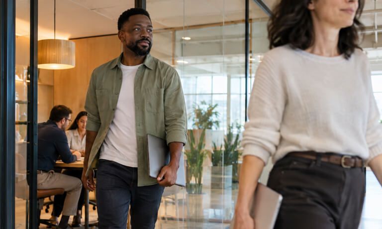 Two colleagues walking through an office, one carrying a laptop.