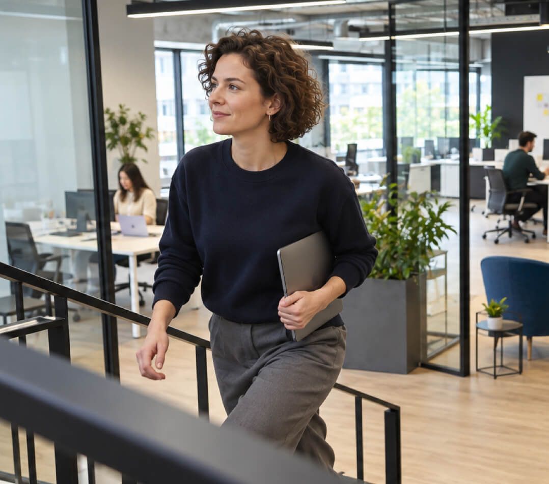 A data scientist with a laptop under her arm walking up the stairs of an open-plan office.